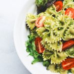Italian Cuisine - Pesto pasta with sliced tomatoes served on white ceramic plate