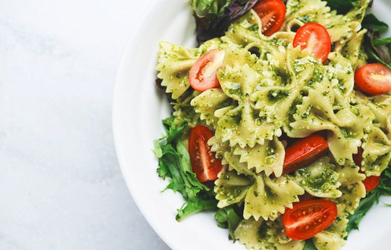 Italian Cuisine - Pesto pasta with sliced tomatoes served on white ceramic plate